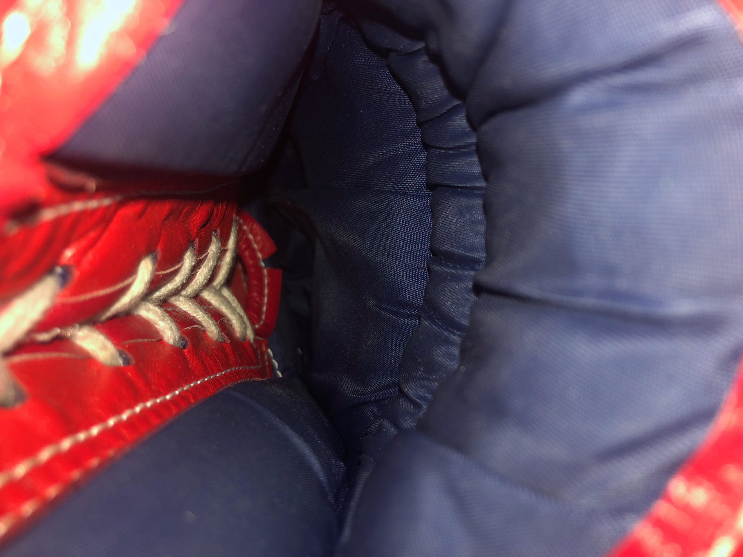 Extreme close up photo of the inside of a boxing glove with red and blue fabric and laces.