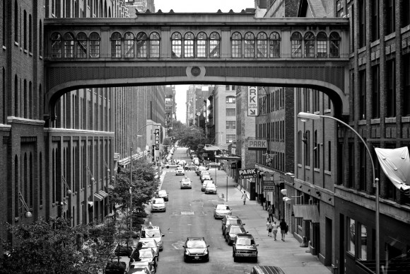 A historic photo of an ornate walkway bridge that connects two city buildings above a street down below.