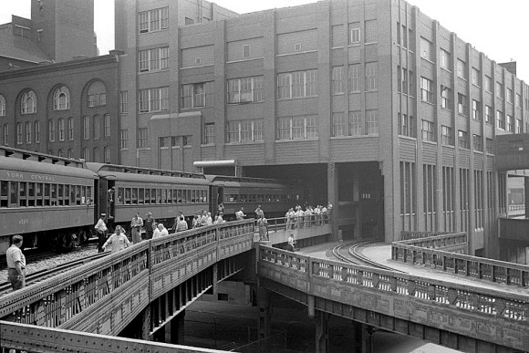 A black and white photo of a building with an elevated railway build into the bottom floor.
