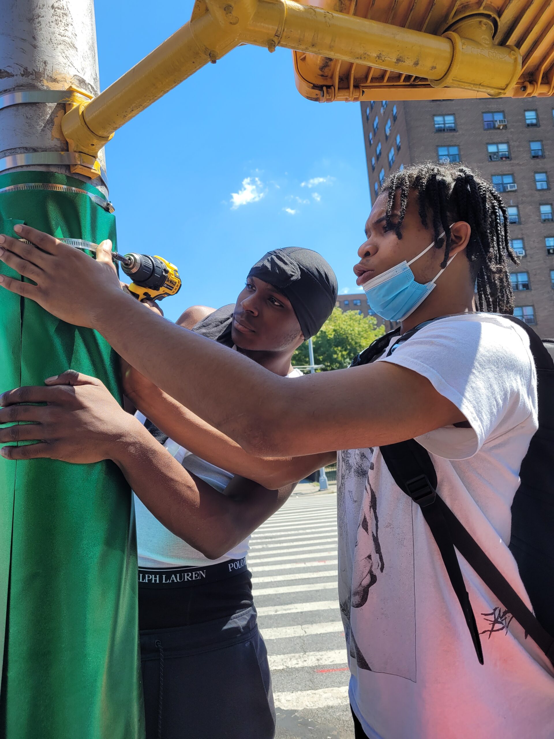 Photo of Esteban and Jamel installing Beyond Memorial prototype on lamp post at Sutter Ave. & Mother Gaston Blvd., Dr. Green Playground in Brownsville.